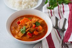 there is a bowl of soup with meat and vegetables in it next to rice on the table