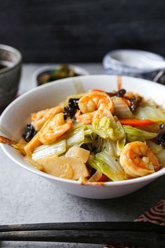 a bowl filled with shrimp and vegetables on top of a table next to chopsticks