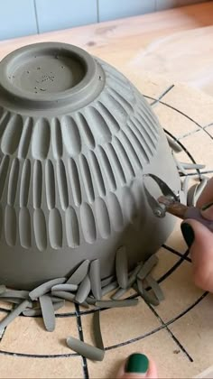 someone is using scissors to cut out the bottom of a clay vase with holes in it