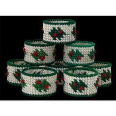 six white and green knitted baskets with holly decorations on them, all stacked together