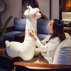 a woman sitting on a couch petting a stuffed llama