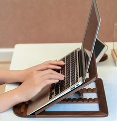 a person using a laptop computer on a wooden stand in front of a white table