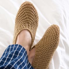 a person's feet wearing slippers on top of a white bed with a blue checkered shirt