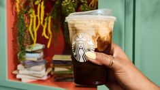 a person holding up a starbucks drink in front of a green cabinet with flowers on it