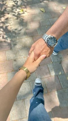 two people holding hands while standing next to each other on a brick walkway with trees in the background