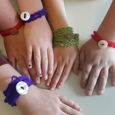 four children's hands with different colored bracelets on top of a white table