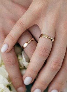 two hands holding each other with wedding rings on top of them and white flowers in the background