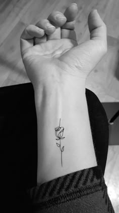 a black and white photo of a woman's wrist with a single rose tattoo on it