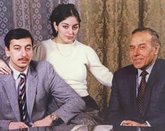 two men and a woman sitting next to each other in front of curtained windows