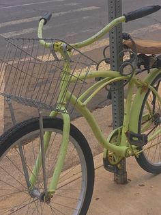 a green bicycle is parked next to a pole on the sidewalk near an empty street