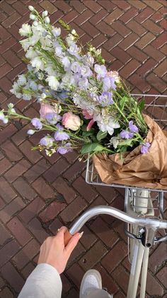 a person on a bike with flowers in the basket and someone's hand reaching for it