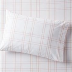 a white and pink plaid pillow on top of a bed next to a beige checkered wall