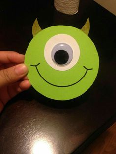 a hand holding up a green paper cutout with a monster's eyes