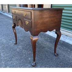 an old wooden desk with gold decorations on the top and legs, sitting in front of a building