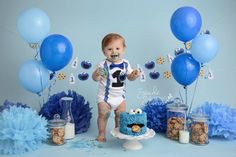 a baby boy standing in front of blue balloons and cake