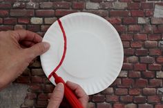 a person is holding a paper plate with a red string on it, and another hand is pulling the edge off