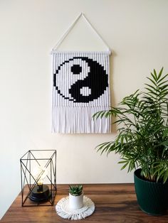 a wall hanging with a black and white design on it next to a potted plant