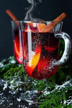 two mugs filled with liquid and cinnamon sticks on top of snow covered ground next to plants