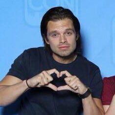 a man making a heart shape with his hands while standing in front of a blue background