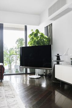 a flat screen tv sitting on top of a wooden floor in a living room next to a window