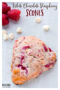 white chocolate raspberry scones on a piece of parchment paper next to some raspberries