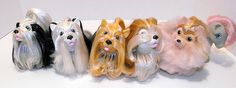 five small dog figurines are lined up on a white counter top, one is wearing a pink hat and the other has long hair