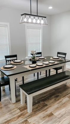 a dining room table with black chairs and white plates on it, next to a bench