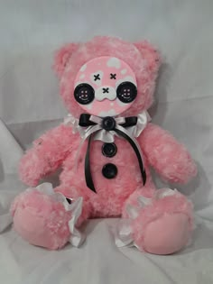 a pink teddy bear sitting on top of a white sheet with buttons in it's eyes