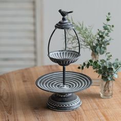 two tiered metal trays sitting on top of a wooden table next to a vase