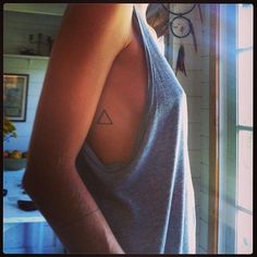 a woman with a triangle tattoo on her upper arm and shoulder, standing in front of a window