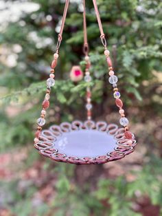 a bird feeder hanging from a tree with beads and chains on it's sides