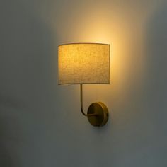 a wall light with a white shade on it's side and a lamp attached to the wall