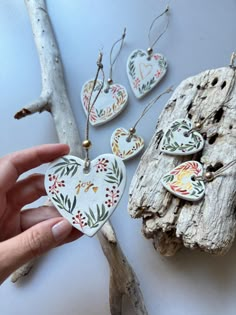 a hand holding a heart shaped ceramic ornament next to some wood and branches