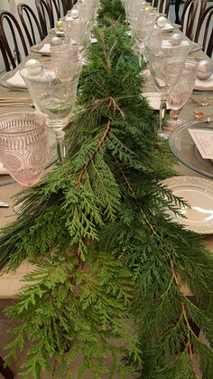 the table is set with pine branches and place settings for two people to sit at