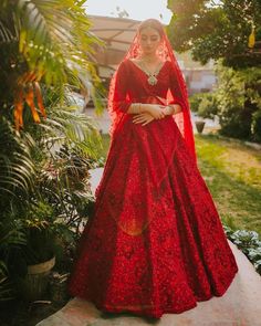 a woman wearing a red wedding gown and veil in the sun with her hands on her hips