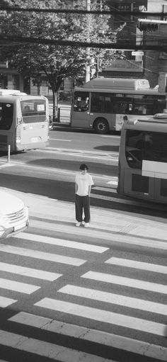 a man standing in the middle of a crosswalk with buses and cars behind him