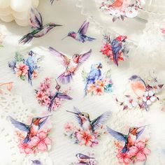 many birds and flowers on a white tablecloth with balloons in the backround