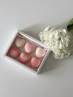 a white hydrangea and pink heart shaped candies in a box next to a flower