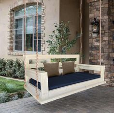 a porch swing with pillows on it and a brick wall in front of the house