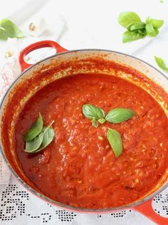 a red pot filled with sauce and basil leaves