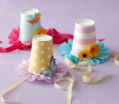 three small hats with ribbons around them on a purple tablecloth, one is decorated with flowers and the other has a butterfly