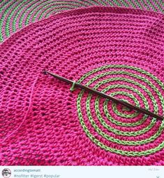 there is a crocheted pink and green rug on the floor next to a knitting needle