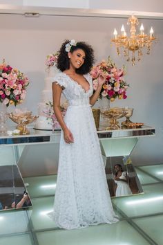 a woman in a white dress standing next to a table with flowers and cake on it