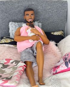 a doll sitting on top of a bed next to pink and gray pillows in a bedroom