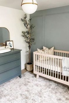 a baby's room with a crib, dresser and tree in the corner