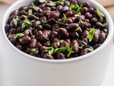 a white bowl filled with black beans and garnished with green leaves on top