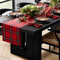 the table is set with red and black place mats, plaid napkins, silverware, and greenery