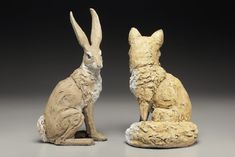 two ceramic rabbits sitting next to each other on a gray surface with black background,