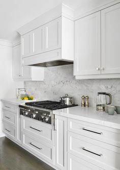 a white kitchen with marble counter tops and stainless steel range hood over the stove top