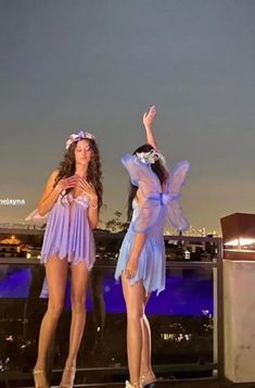 two women dressed in fairy costumes standing next to each other on top of a roof